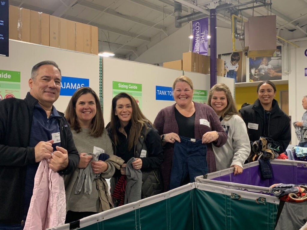 A photo on the Boston area team members of Riskified at the Cradles to Crayons volunteering event holding clothes to sort into bins