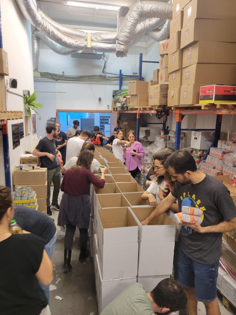 A photo from the Jaffa Institute volunteer event of Riskified team members in a storage room sorting food items into a row of boxes to be distributed to families